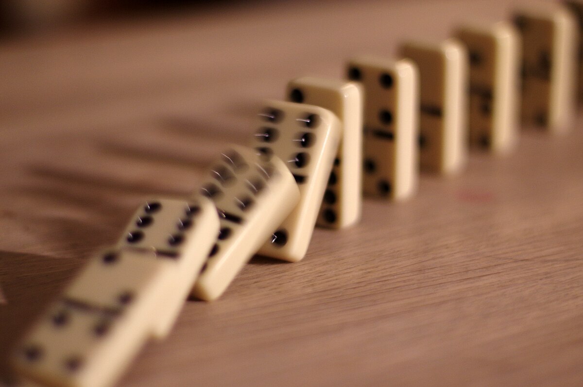 A line of dominoes falling, with several already toppled and others in the process of falling, illustrating the domino effect.