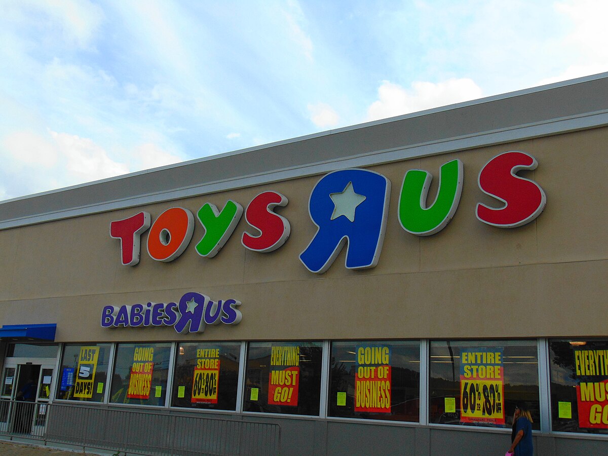 The exterior of a Toys "R" Us and Babies "R" Us store in Auburn, Massachusetts, is shown on June 24, 2018, during its closing sale. The store's prominent colorful logo is visible, along with "GOING OUT OF BUSINESS" and "EVERYTHING MUST GO!" signs displayed in the windows.