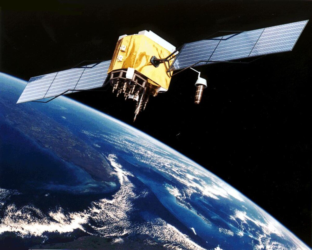 An artistic rendering of a GPS satellite in orbit above Earth, with its solar panels extended. The Earth's surface and clouds are visible below the satellite.