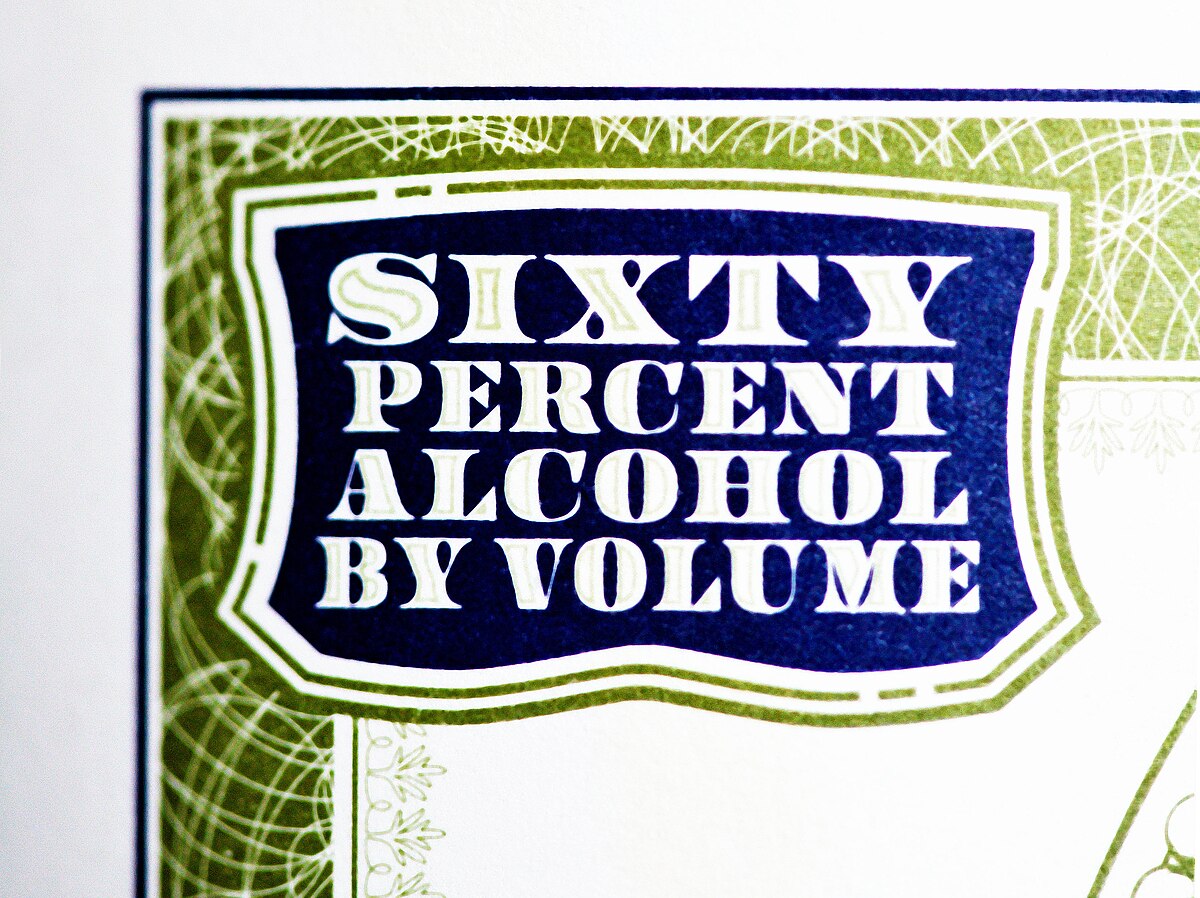 A close-up of a label on a bottle of absinthe, prominently displaying the text "SIXTY PERCENT ALCOHOL BY VOLUME" in a decorative blue and green design. This indicates the alcohol content of the beverage.