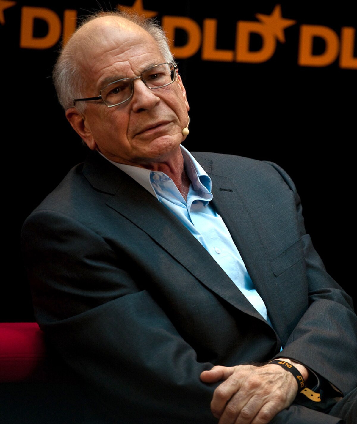 A portrait of Daniel Kahneman shows him wearing glasses and a dark suit with a light blue shirt, seated against a dark background with the DLD logo visible. Kahneman's research established that common human errors can arise from heuristics and biases.