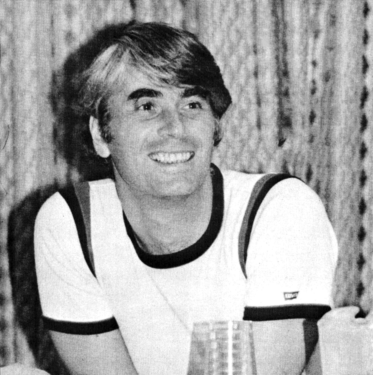 Portrait of philosopher Robert Nozick, featured on the cover of Libertarian Review in 1977. He is smiling and looking to the right, with a casual hairstyle and wearing a t-shirt with stripes on the shoulders.