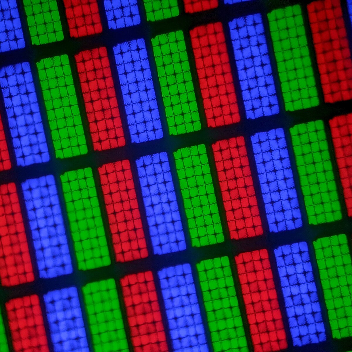 Close-up macro photograph of the subpixels on a Samsung UA40M5860AKCHD TV screen. The image shows a repeating pattern of blue, green, and red rectangular subpixels, each composed of a grid of smaller elements.