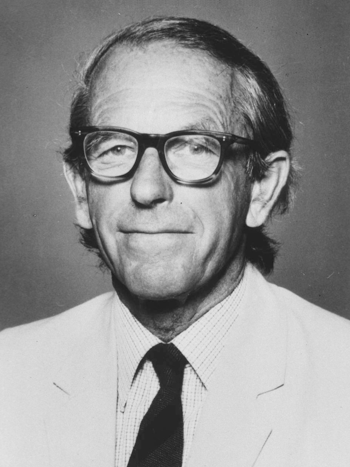 Portrait of Frederick Sanger, a man with glasses and a dark tie, looking directly at the camera. He is known for his pioneering work in sequencing proteins and DNA, for which he received two Nobel Prizes.