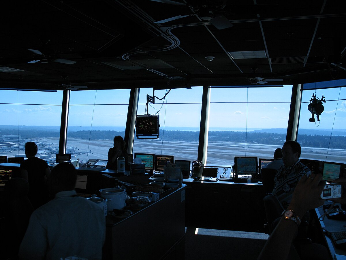 The interior of the Seattle–Tacoma International Airport control tower, showing air traffic controllers at their stations with radar displays and other equipment. The tower, commissioned in 2004, is 850 sq ft (79 sq m) and features a light gun in the upper right.