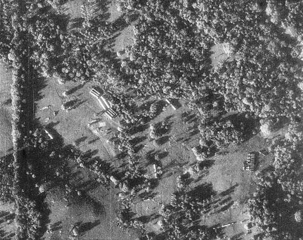 A black and white reconnaissance photograph from the Cuban Missile Crisis shows a missile site with several long, cylindrical objects identified as missiles, surrounded by trees and clearings. This image was taken by a U-2 spy plane.