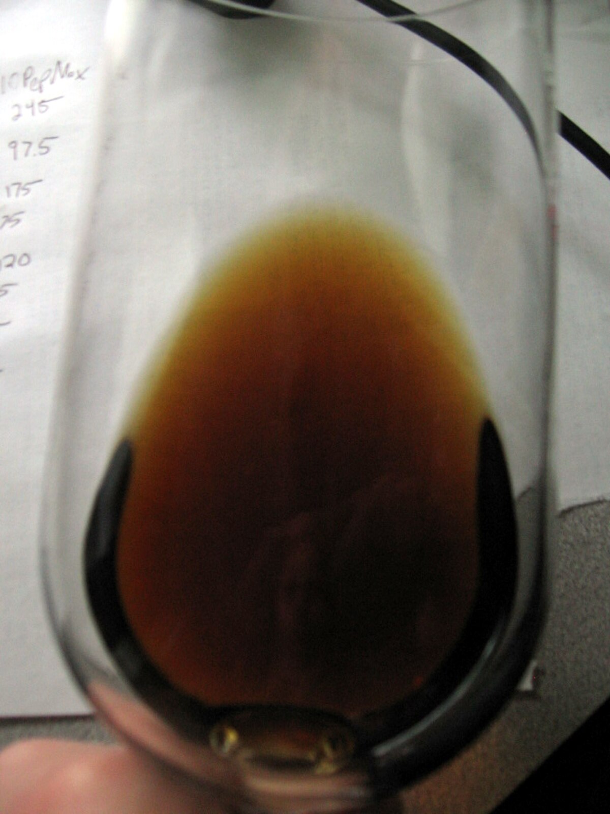A glass containing aged Malmsey Madeira wine, exhibiting a deep brown color. The color change is characteristic of white wines as they age.