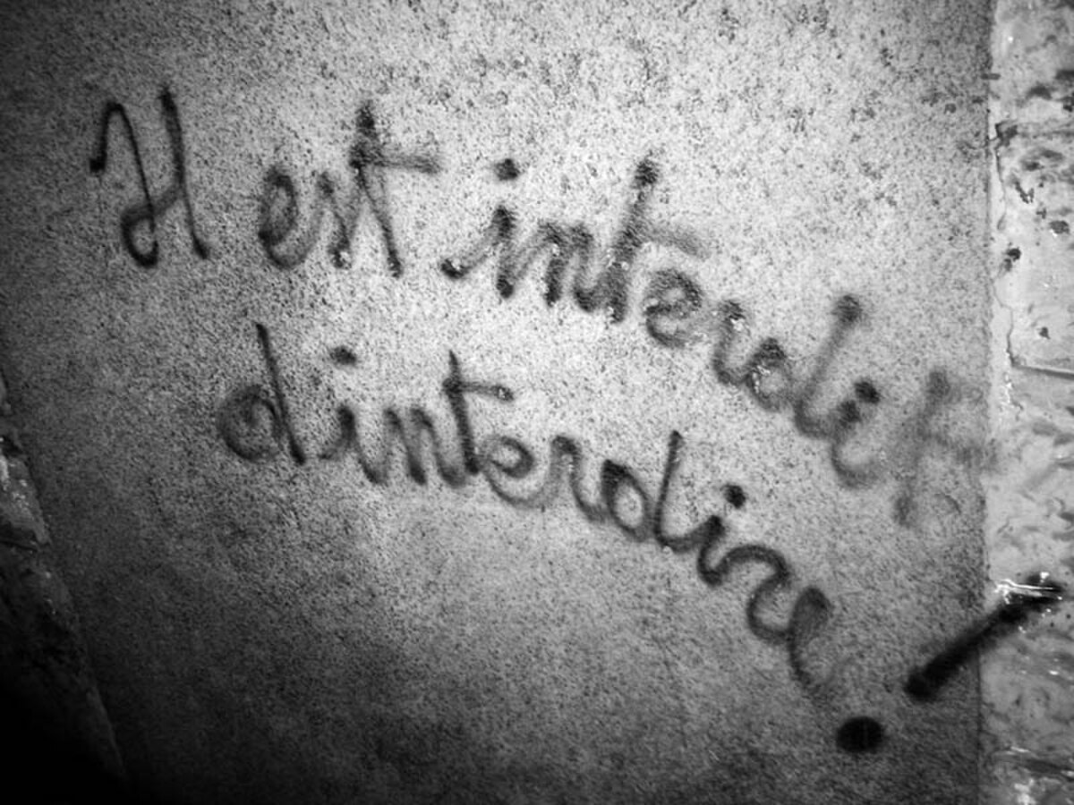 Black and white photograph of graffiti on a wall, reading "Il est interdit d'interdire!" which translates to "It is forbidden to forbid!". This slogan was prominent during the May 1968 protests in France.