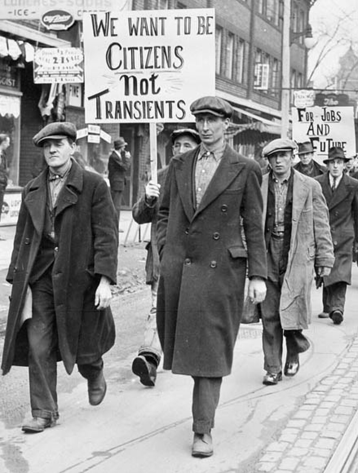 Black and white photograph of unemployed men marching in Toronto, Ontario, Canada, during the Great Depression. One man in the foreground holds a sign that reads "WE WANT TO BE CITIZENS Not TRANSIENTS," while another sign in the background reads "FOR JOBS AND FUTURE."