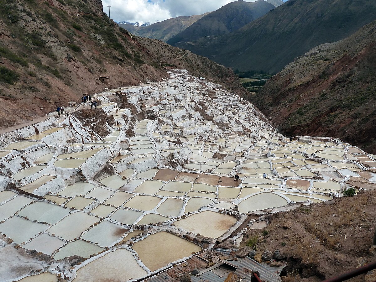 Terraced salt evaporation ponds, known as Salinas de Maras, are carved into a mountainside near Maras, Peru. These ponds, fed by a mineral spring, have been used for salt production since pre-Inca times, with people visible walking along the paths.