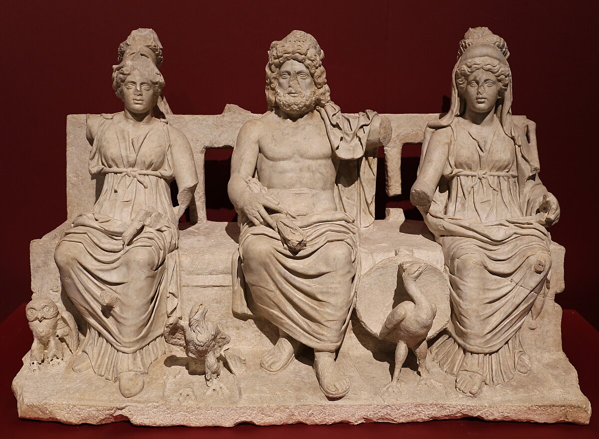 A marble sculpture of the Capitoline Triad, depicting Jupiter enthroned in the center, flanked by Juno on the left and Minerva on the right. Jupiter holds a scepter and is accompanied by an eagle, while Juno has a peacock and Minerva has an owl, dating from 160-180 AD.